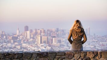 A woman sitting on a stone wall overlooking a city skyline