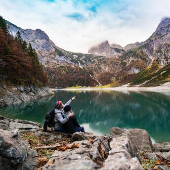 Two hikers pointing at a mountain across a serene lake in autumn