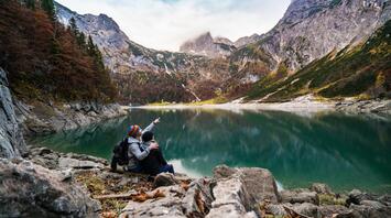 Two hikers pointing at a mountain across a serene lake in autumn