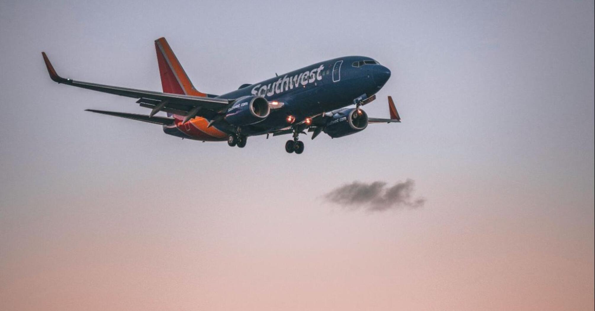 A Southwest Airlines plane descending over palm trees and a city skyline during sunset