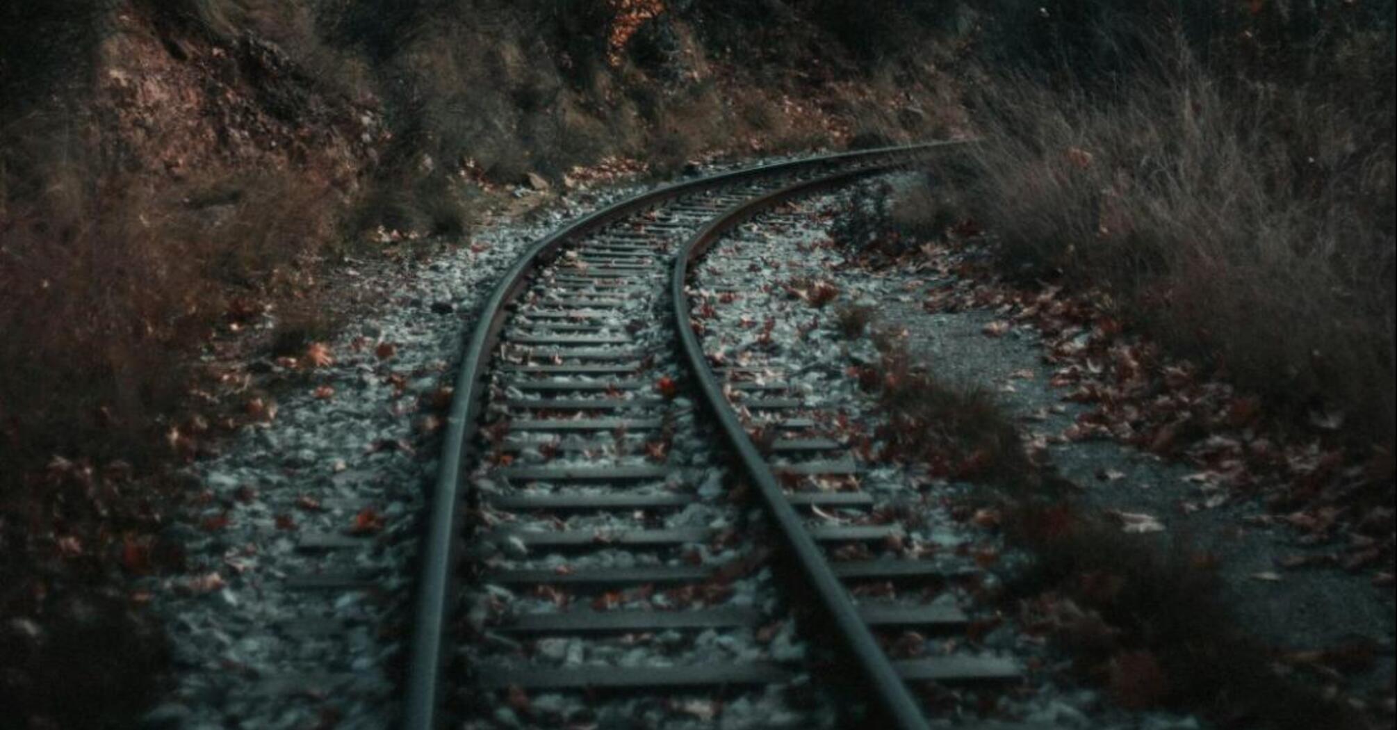 A curved railway track cutting through a forest with autumn foliage