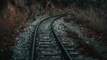 A curved railway track cutting through a forest with autumn foliage