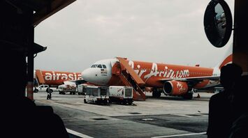 An AirAsia plane is parked on the tarmac at an airport, with cargo being loaded in preparation for a flight
