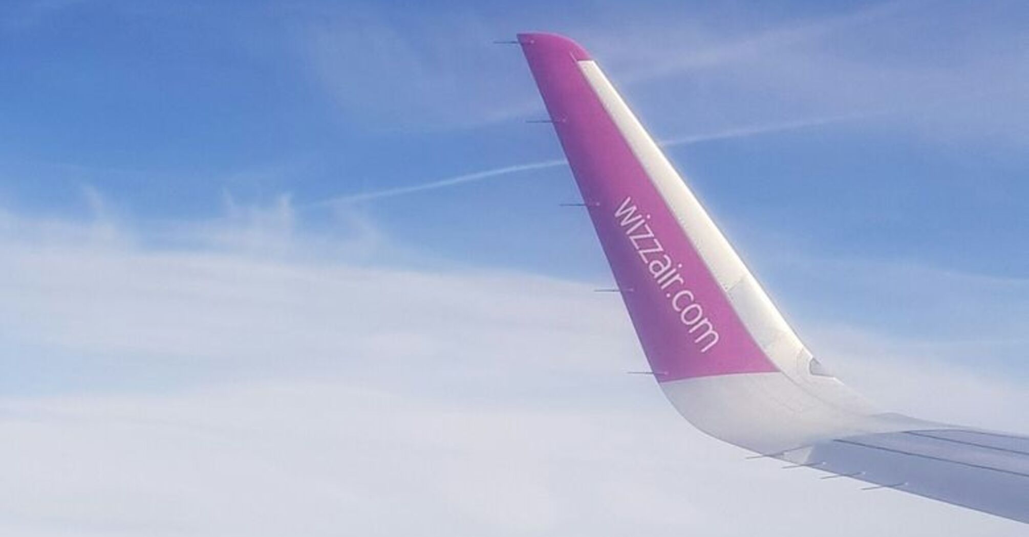 Aerial view of green landscape with a Wizz Air airplane wing visible in the sky