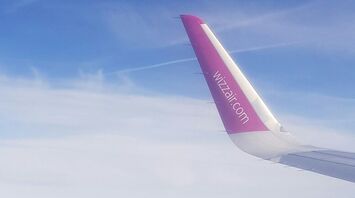 Aerial view of green landscape with a Wizz Air airplane wing visible in the sky