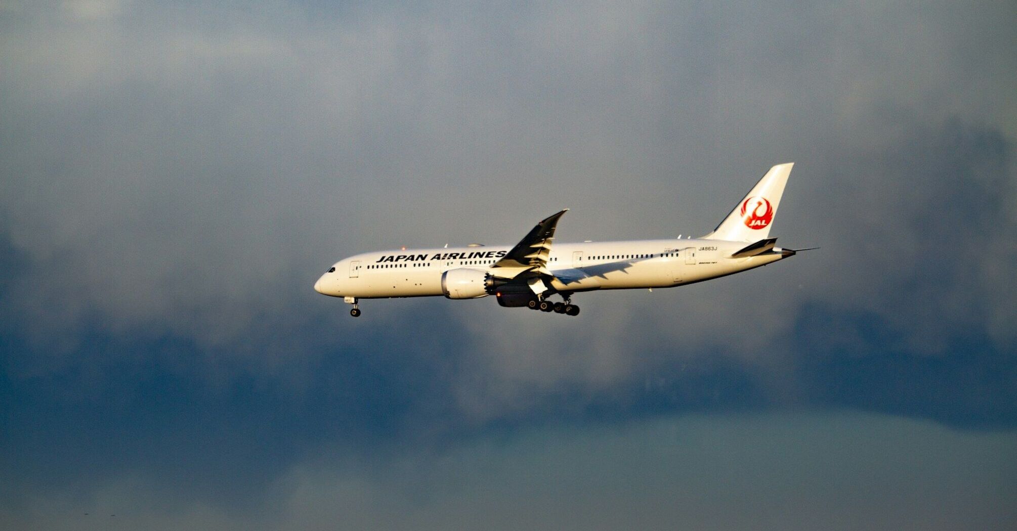 Japan Airlines aircraft in flight during approach, against a cloudy sky