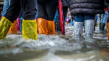 People wading through flooded streets wearing colorful waterproof boots