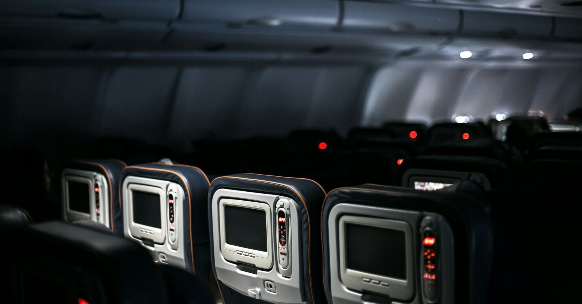 Empty seats and entertainment screens inside a dimly lit airplane cabin