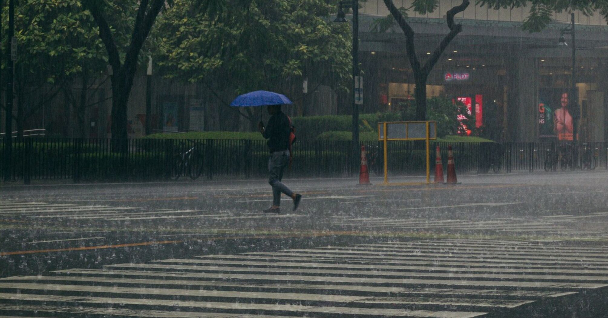 A person with an umbrella walking across a street during heavy rain under traffic lights in a city