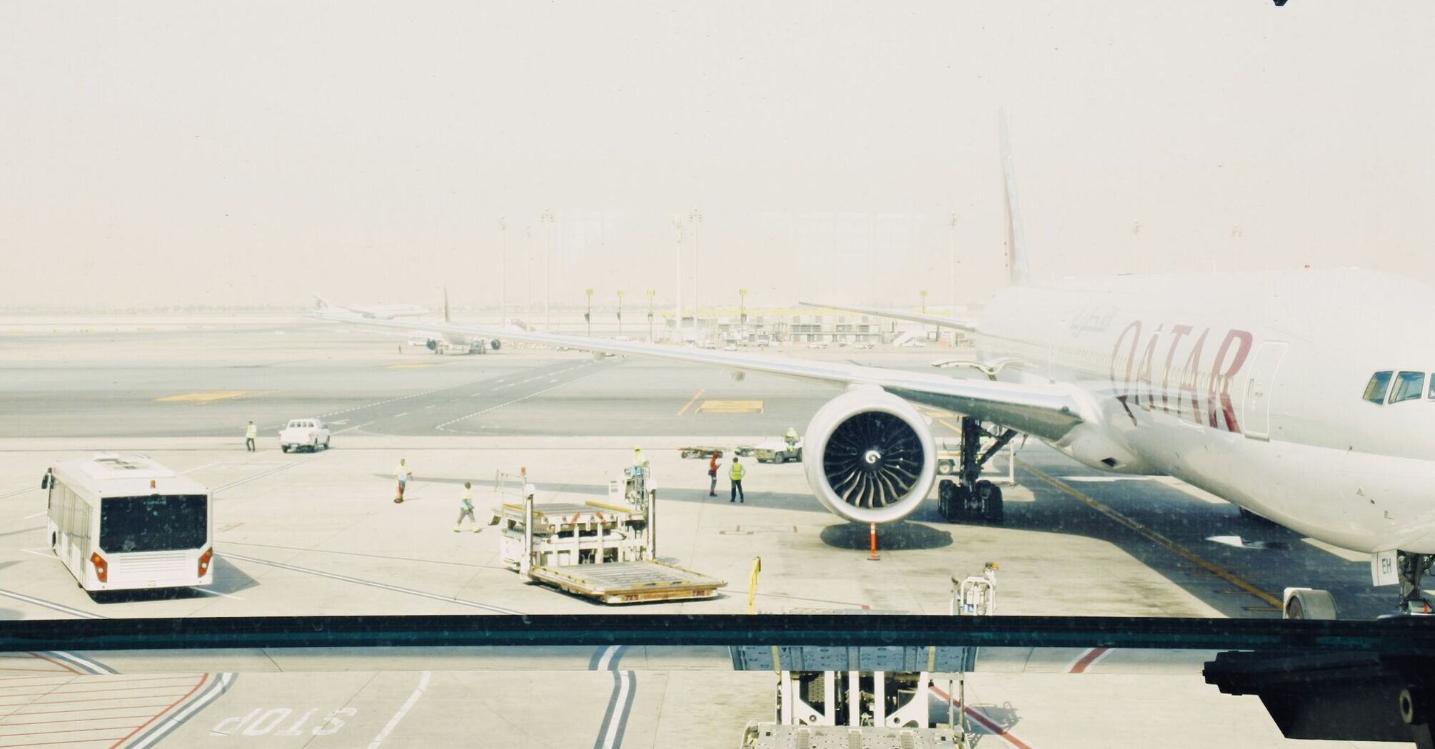 Qatar Airways plane on the runway at an airport, with ground staff and equipment nearby