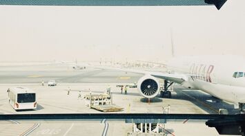 Qatar Airways plane on the runway at an airport, with ground staff and equipment nearby
