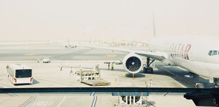 Qatar Airways plane on the runway at an airport, with ground staff and equipment nearby
