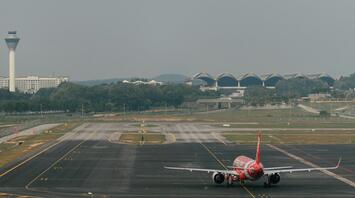 A red AirAsia airplane taxiing on the runway at an airport with a control tower and terminal buildings in the background