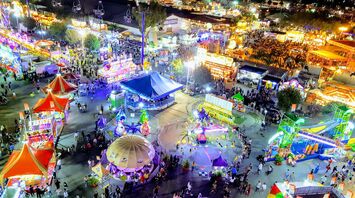 A vibrant nighttime view of a fair showcasing colorful rides, food stalls, and visitors enjoying the event