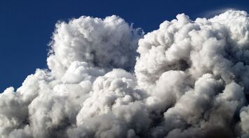 Thick clouds of smoke rise against a blue sky