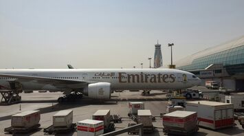 Emirates airplane stationed at the airport terminal, with cargo containers and airport equipment visible in the foreground
