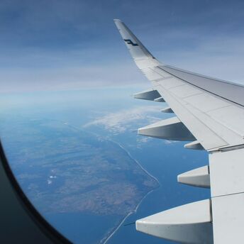 View from an airplane window showing the wing and coastline below