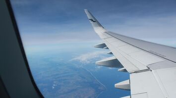 View from an airplane window showing the wing and coastline below
