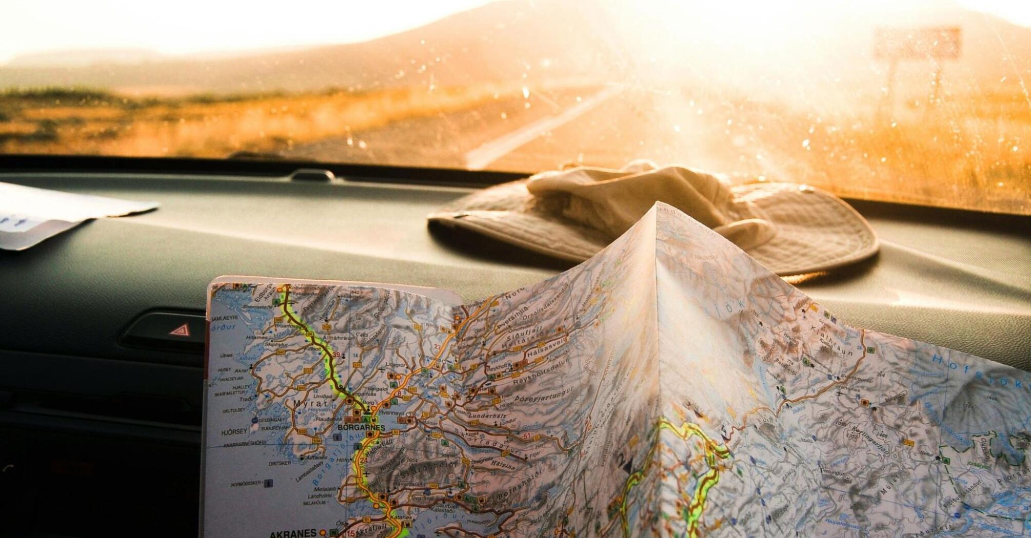 A close-up of a road map being held in a car with sunlight streaming through the windshield, indicating a travel journey