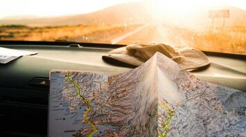 A close-up of a road map being held in a car with sunlight streaming through the windshield, indicating a travel journey