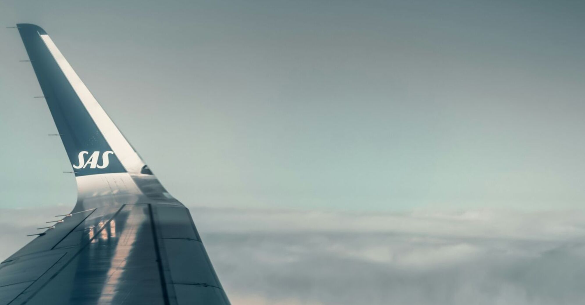 View from an airplane wing mid-flight above the clouds with SAS logo visible