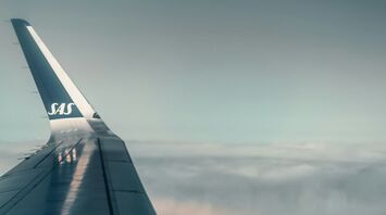 View from an airplane wing mid-flight above the clouds with SAS logo visible