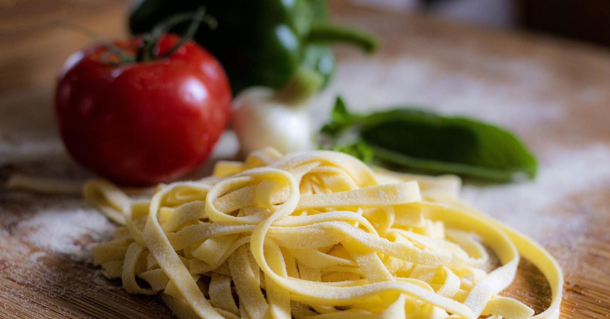 Freshly made pasta with tomatoes and other ingredients on a wooden surface