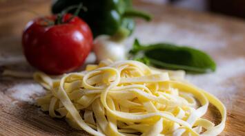 Freshly made pasta with tomatoes and other ingredients on a wooden surface