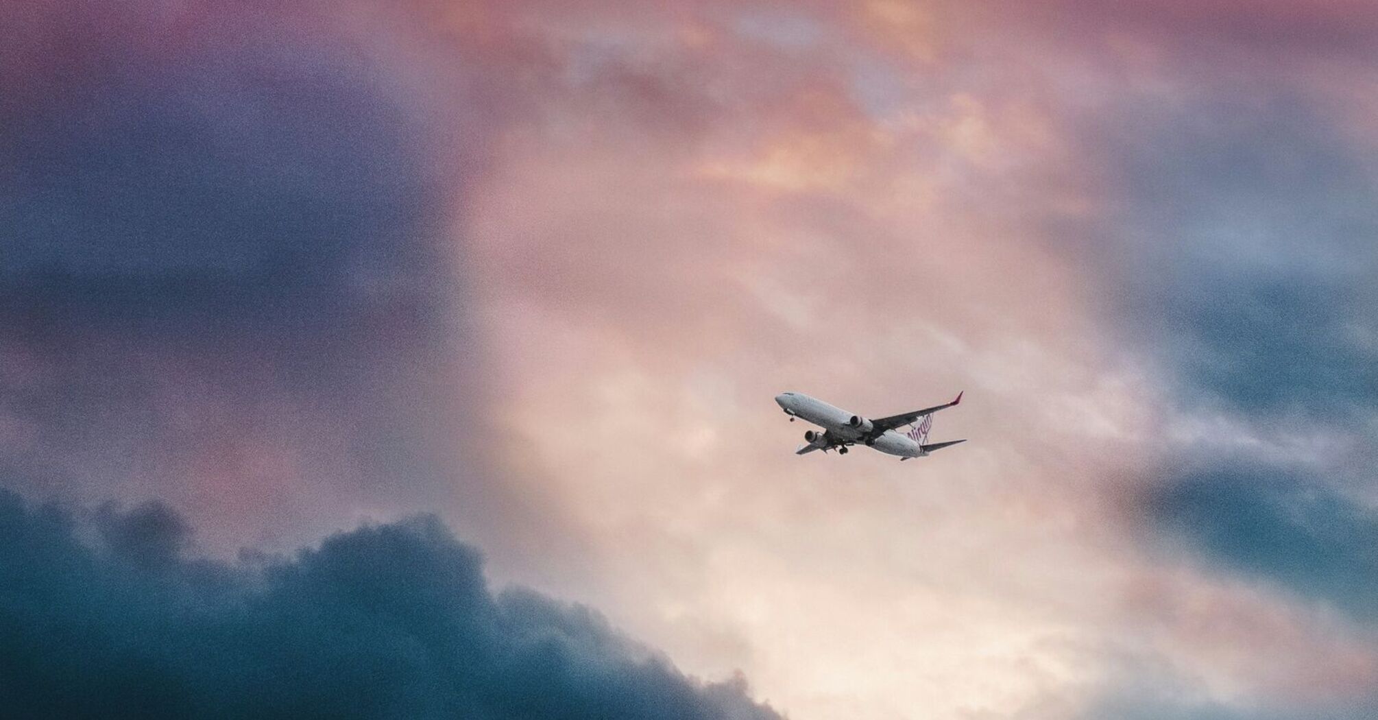 An airplane flies through a vibrant sky with dramatic clouds during sunset