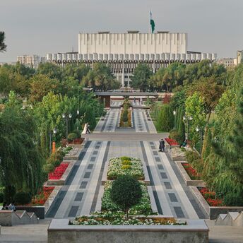 A beautifully landscaped park in Tashkent, Uzbekistan, with neatly arranged flower beds, paved pathways, and the Uzbekistan State Museum of History in the background