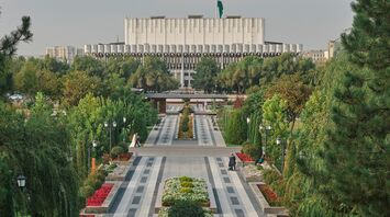 A beautifully landscaped park in Tashkent, Uzbekistan, with neatly arranged flower beds, paved pathways, and the Uzbekistan State Museum of History in the background