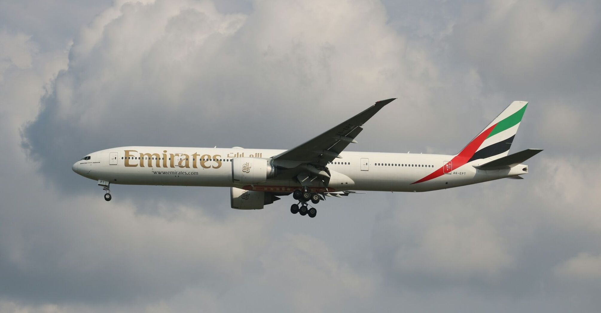 Emirates aircraft flying mid-air against a cloudy sky backdrop