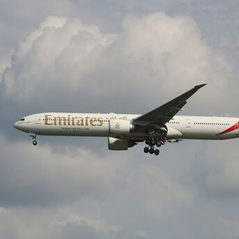 Emirates aircraft flying mid-air against a cloudy sky backdrop