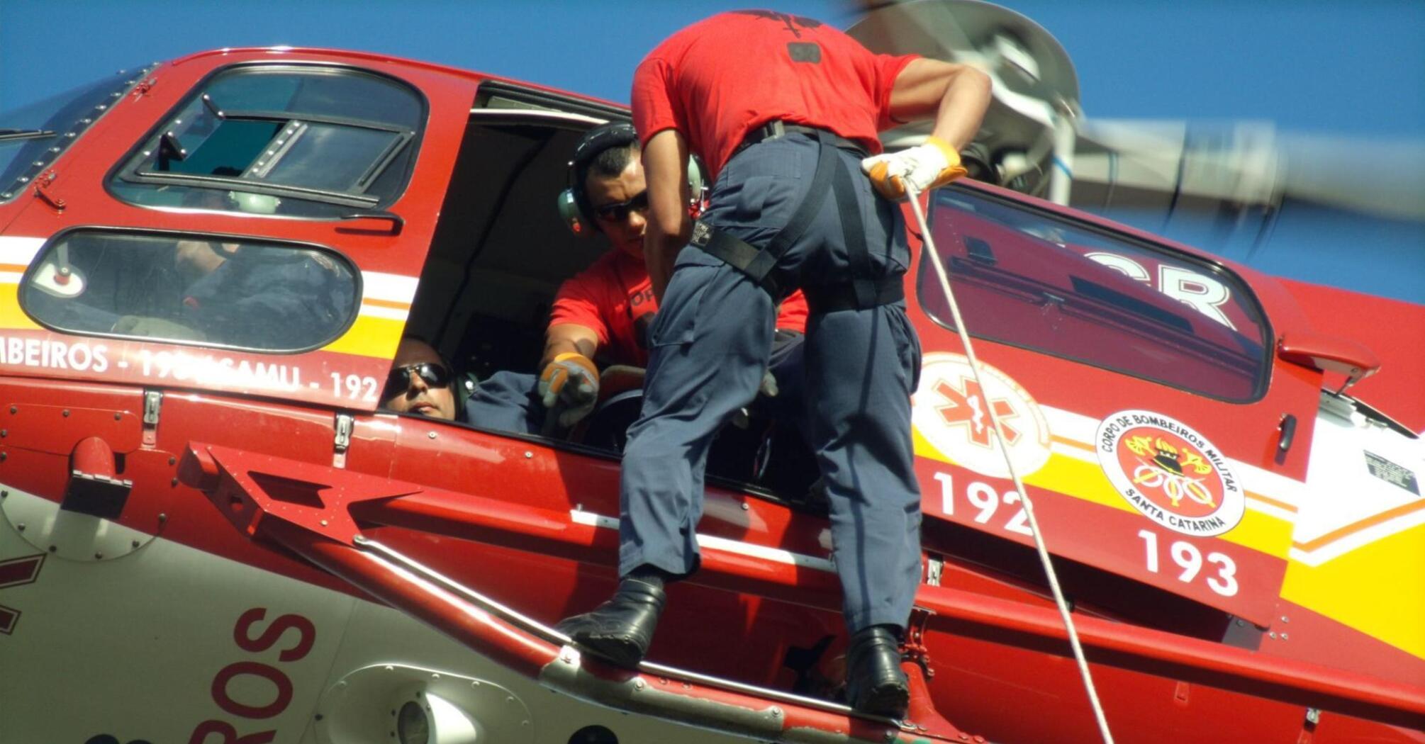 A rescue worker assists from a helicopter during an emergency operation, preparing to hoist someone on board