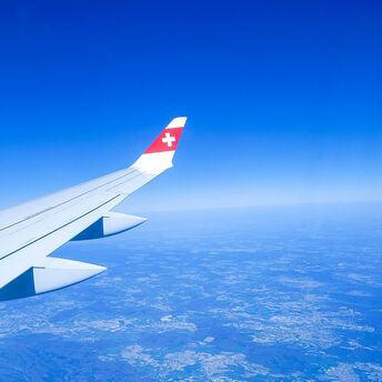 A SWISS Airlines wing in flight, soaring above the landscape with clear blue skies