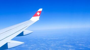 A SWISS Airlines wing in flight, soaring above the landscape with clear blue skies