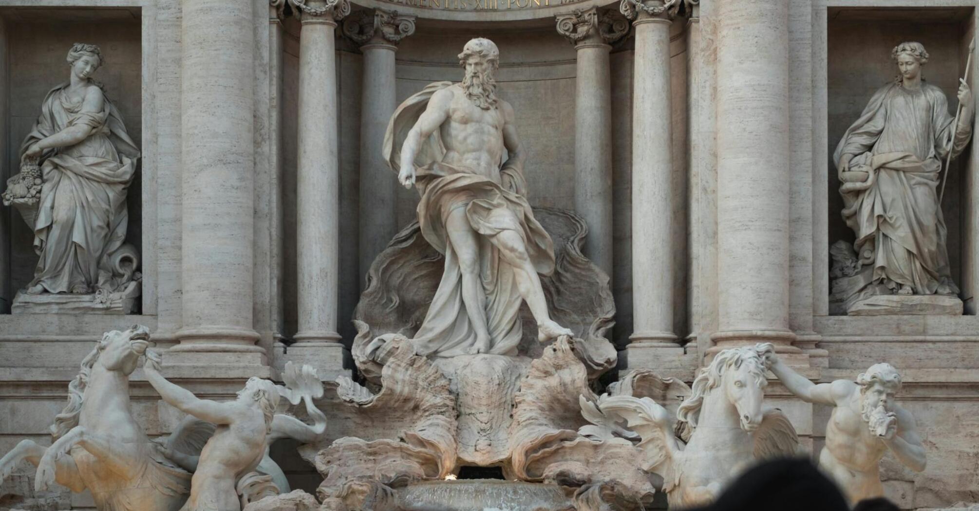 A crowd of tourists in front of the majestic Trevi Fountain in Rome, with statues and sculptures in the foreground