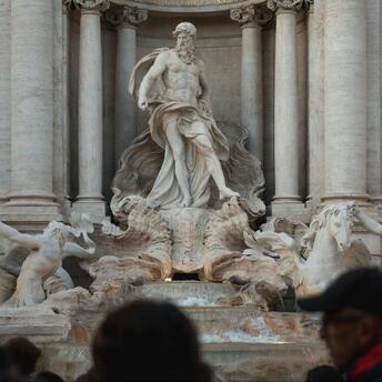 A crowd of tourists in front of the majestic Trevi Fountain in Rome, with statues and sculptures in the foreground
