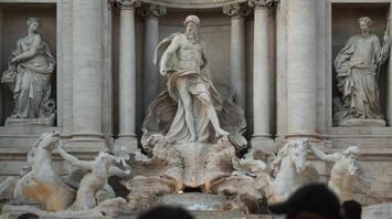 A crowd of tourists in front of the majestic Trevi Fountain in Rome, with statues and sculptures in the foreground