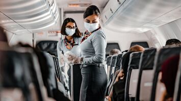 Flight attendants in a plane cabin wearing masks and gloves, serving passengers