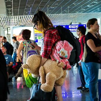 A traveler waiting at the airport, holding a large teddy bear