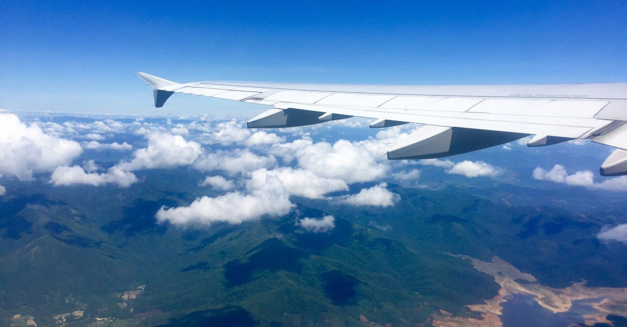 View of a plane's wing flying over a mountainous landscape under a clear blue sky