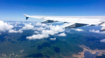 View of a plane's wing flying over a mountainous landscape under a clear blue sky