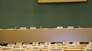 Empty conference chairs with nameplates of countries at an international forum, including UN signage