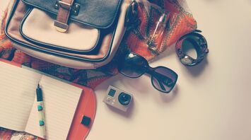 Bag with travel accessories: sunglasses, camera, notebook, and pen
