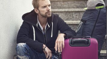 Man sitting with suitcase and backpack on steps