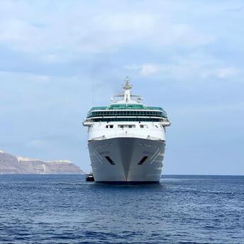 A large cruise ship sailing on calm waters with distant rocky islands in the background under a partly cloudy sky
