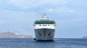 A large cruise ship sailing on calm waters with distant rocky islands in the background under a partly cloudy sky