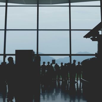Silhouettes of passengers waiting at an Noi Bai Airport terminal with large windows, mountain landscape visible in the background
