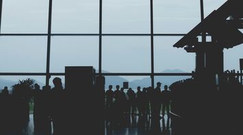 Silhouettes of passengers waiting at an Noi Bai Airport terminal with large windows, mountain landscape visible in the background